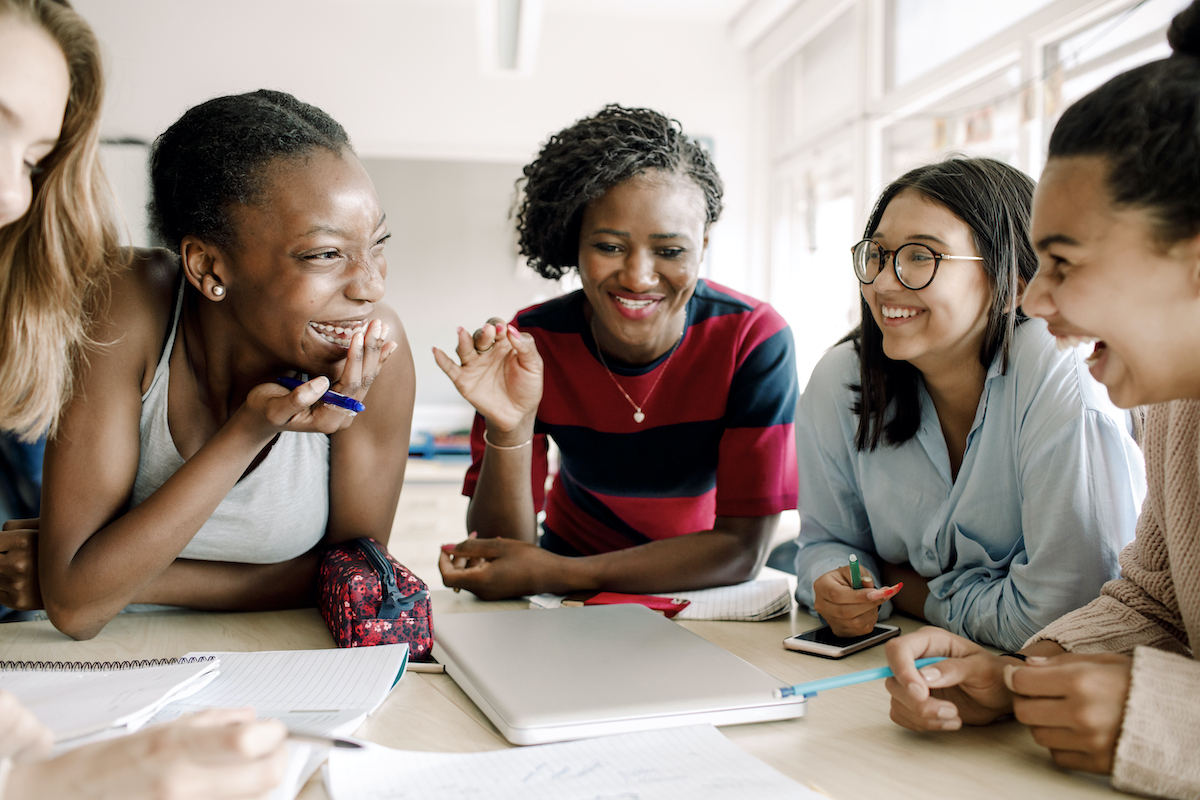 A group of learners from different ethnicities laughing around a classroom table as they learn