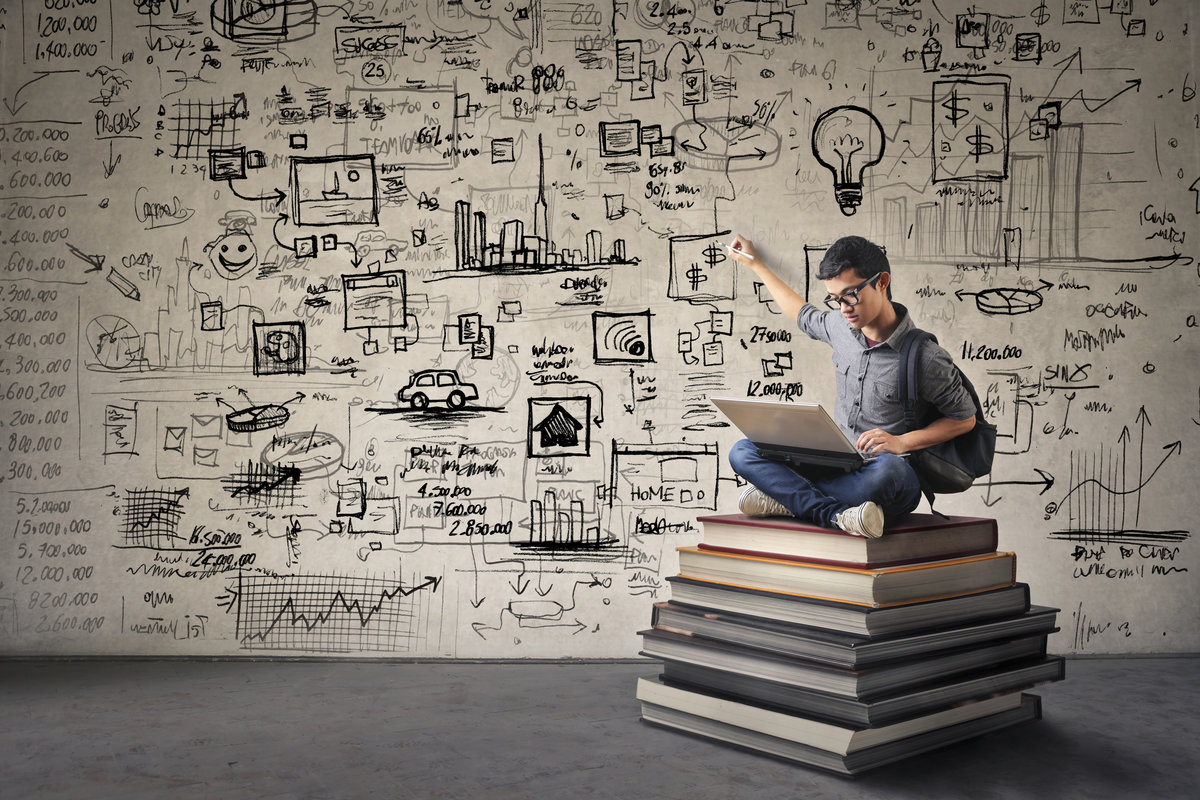 Man sitting on a pile of books drawing images on a wall behind him