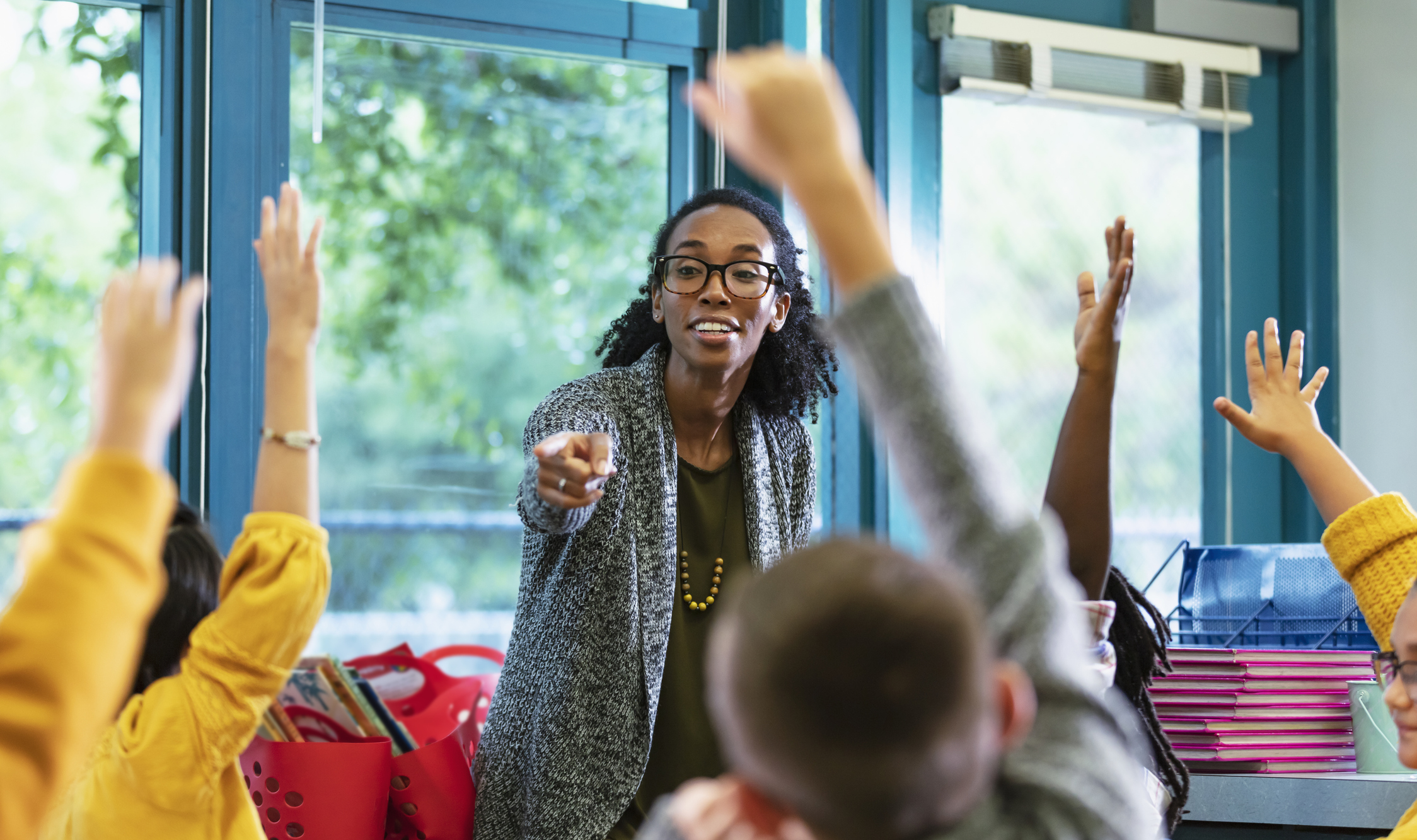 A teacher points at a student with their hand up in the classroom