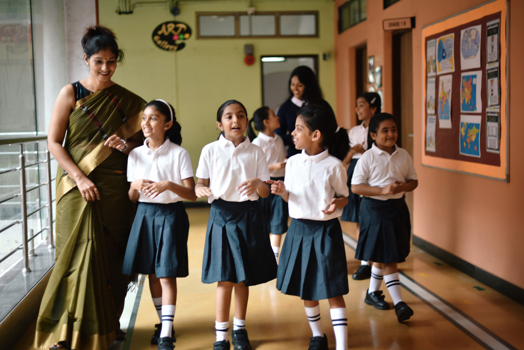 Female teacher and her young students walking happily down a corridor in a school in India