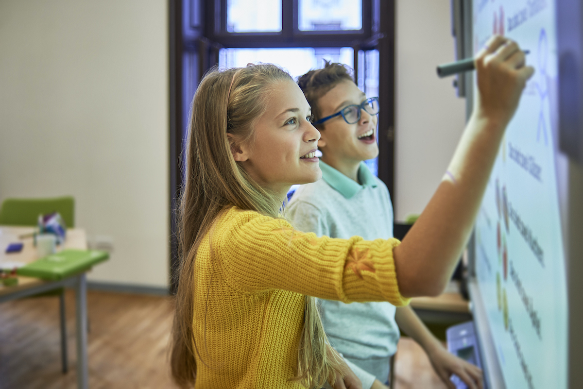 Two young teenagers writing on an interactive whiteboard