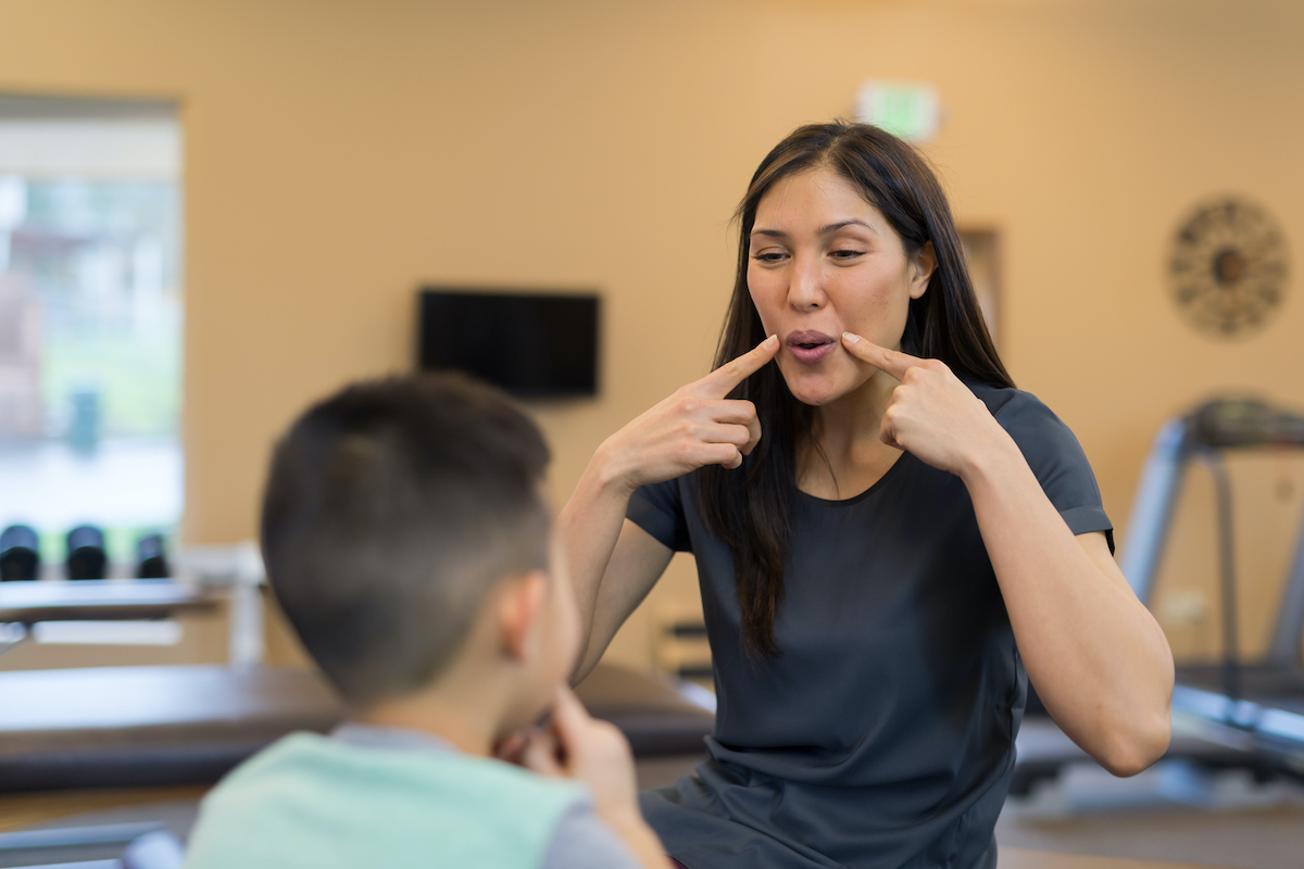 A female teacher showing a student how to make a sound with his mouth.