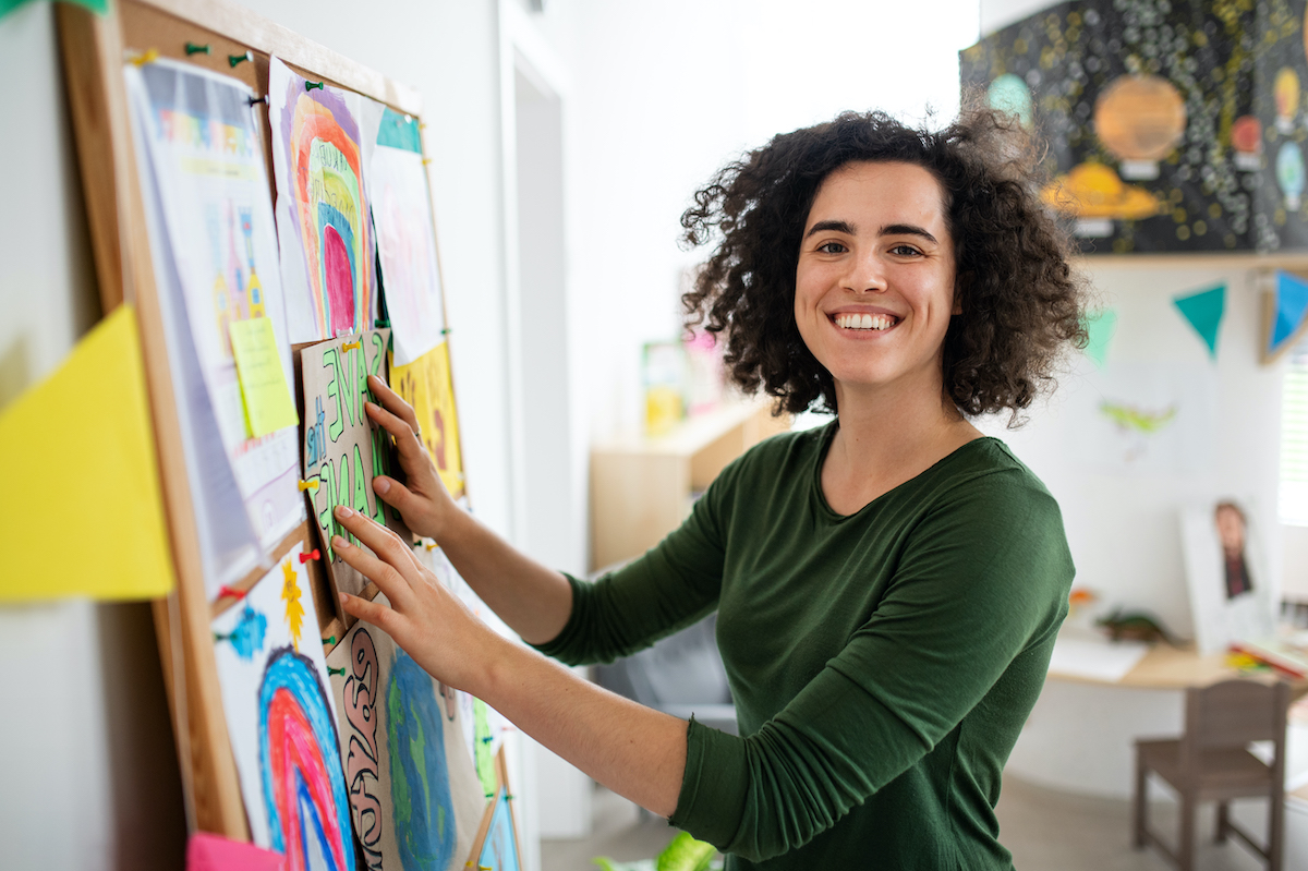 A female teacher standing at a notice board smiling at the camera