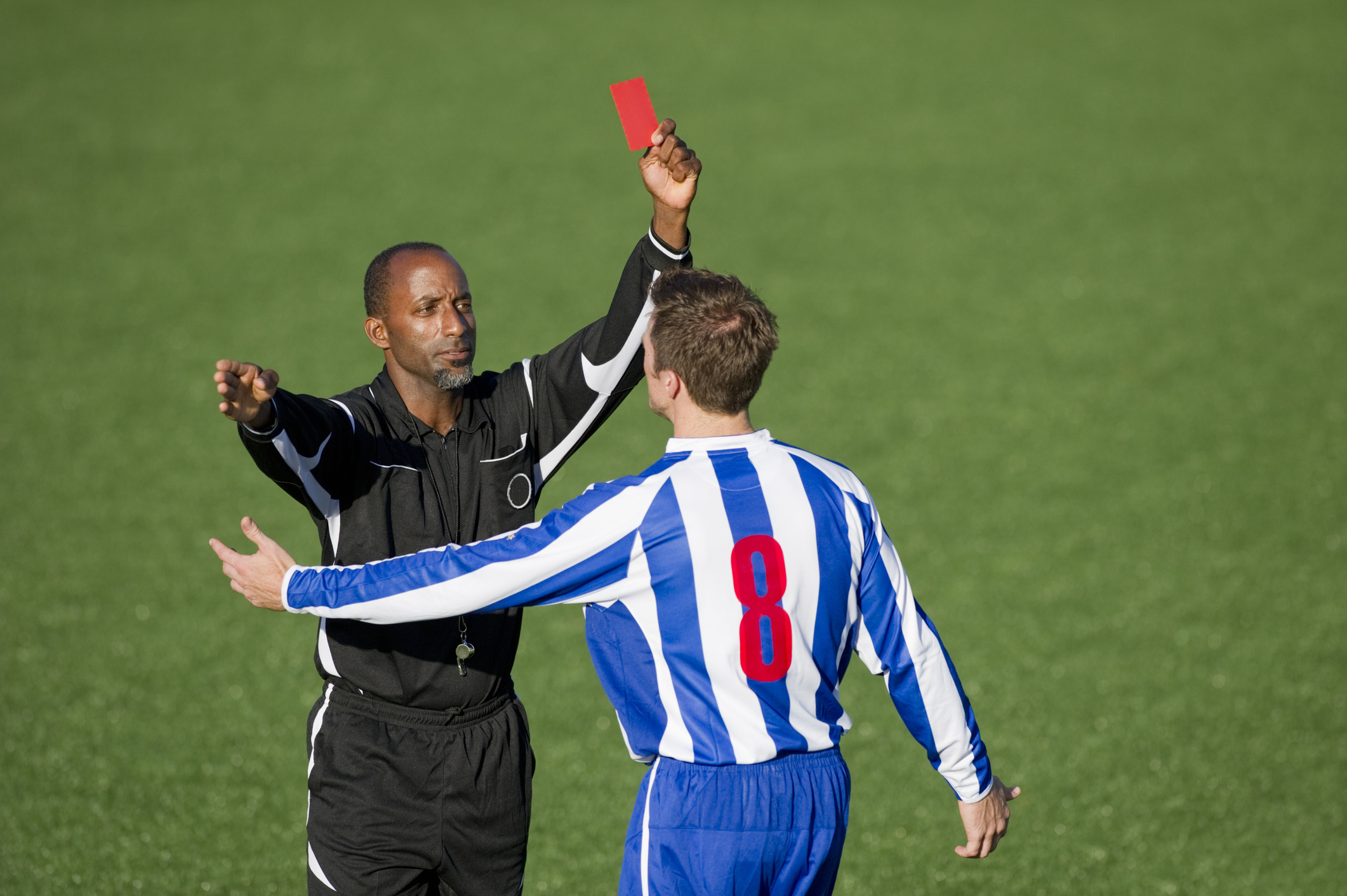 A Black football referee showing a red card to a football player