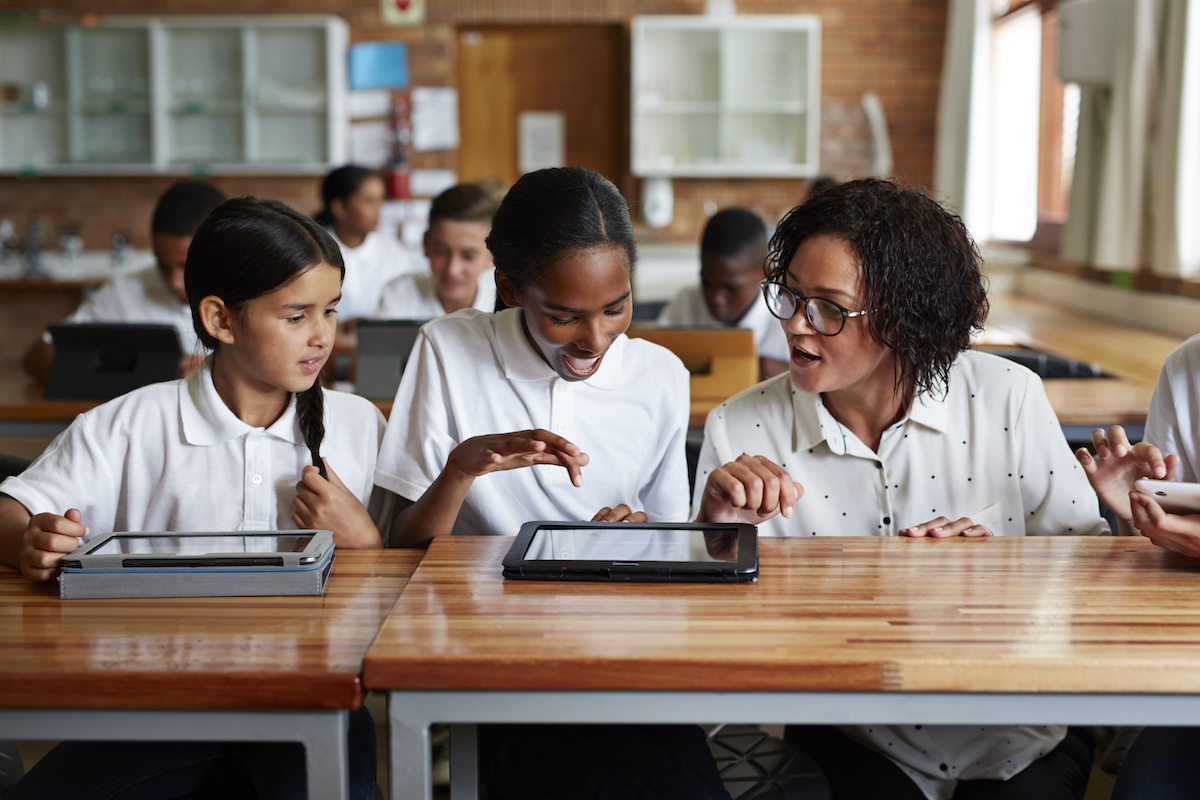 Smiling students and teacher with tablet sitting at a table