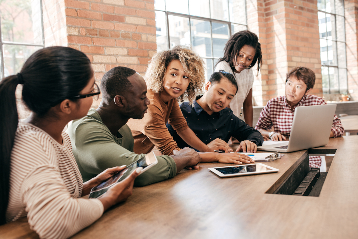 Group of teachers sitting at a table in discussion in from of a laptop computer