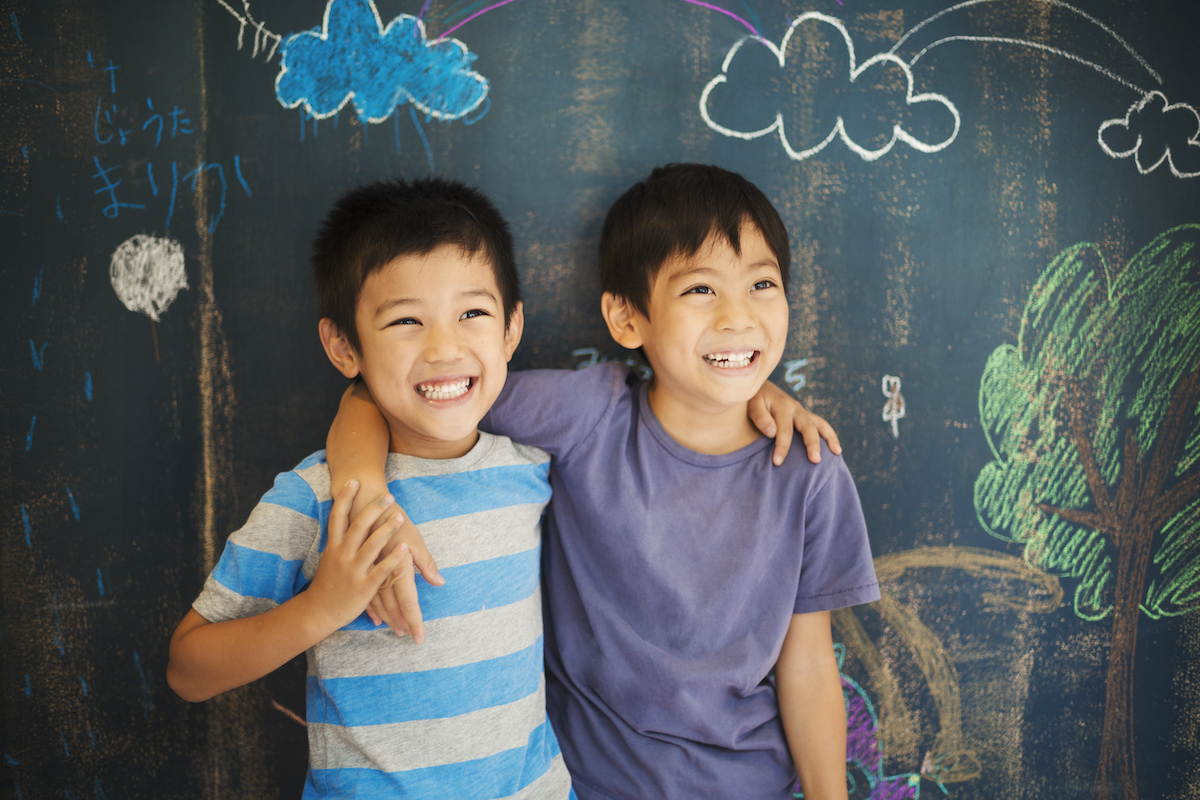 Children in school. Two boys standing with their arms around each others shoulders by a chalkboard