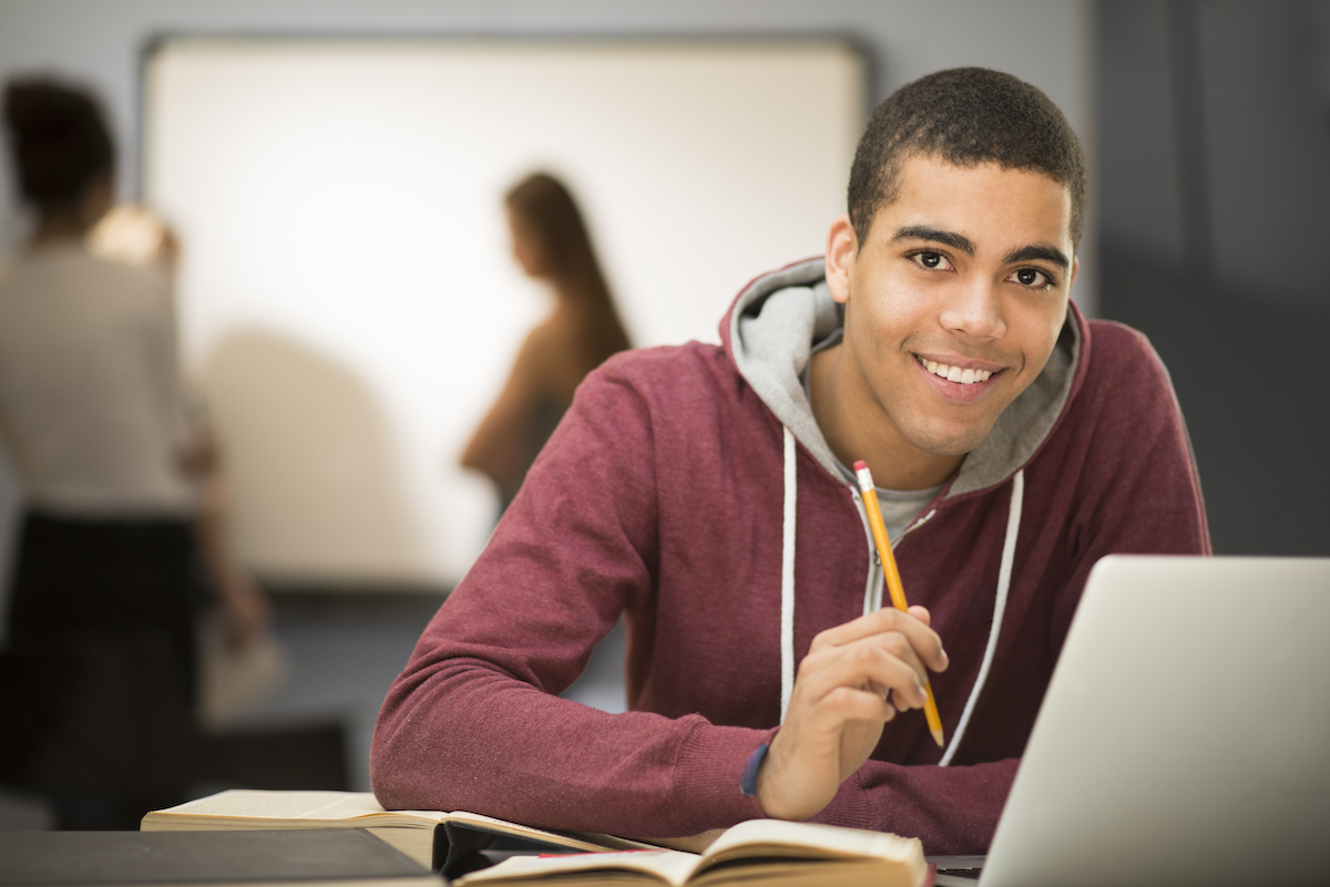 A learner studying in a classroom with his laptop and coursebooks 