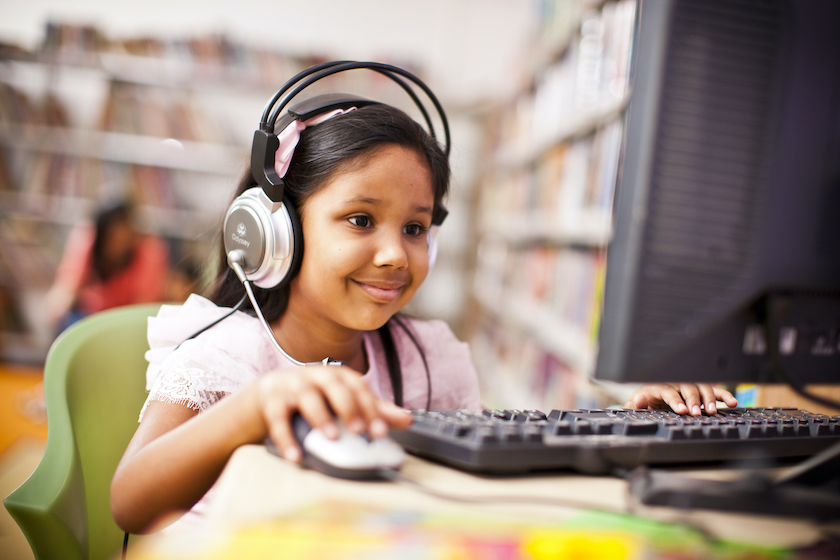 A young girl with headphones on looking at a computer screen