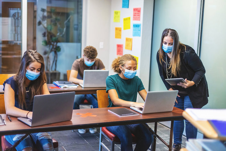 A teacher and three students with face masks looking at computers