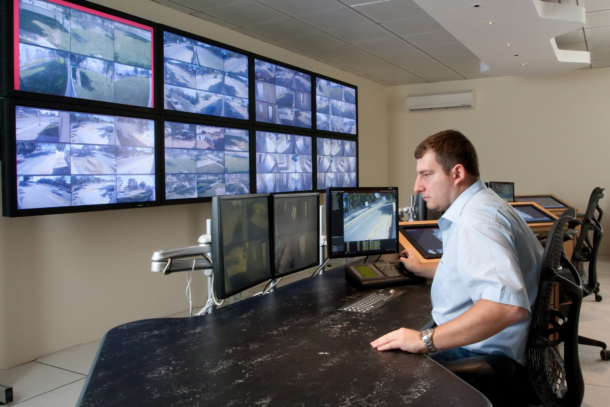 A man is sitting in front of several surveillance screens