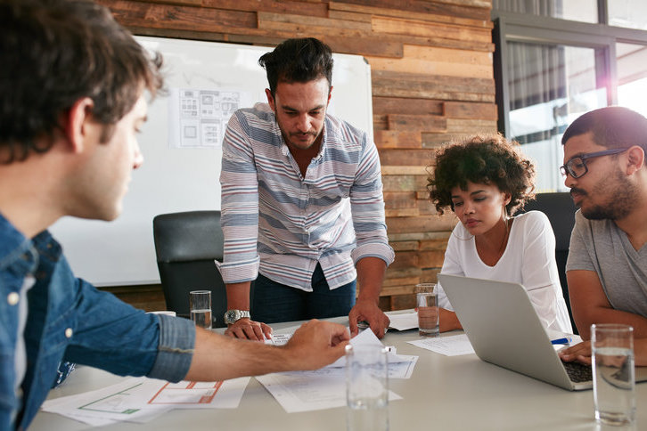 four people discussing work at a table and looking at a laptop computer