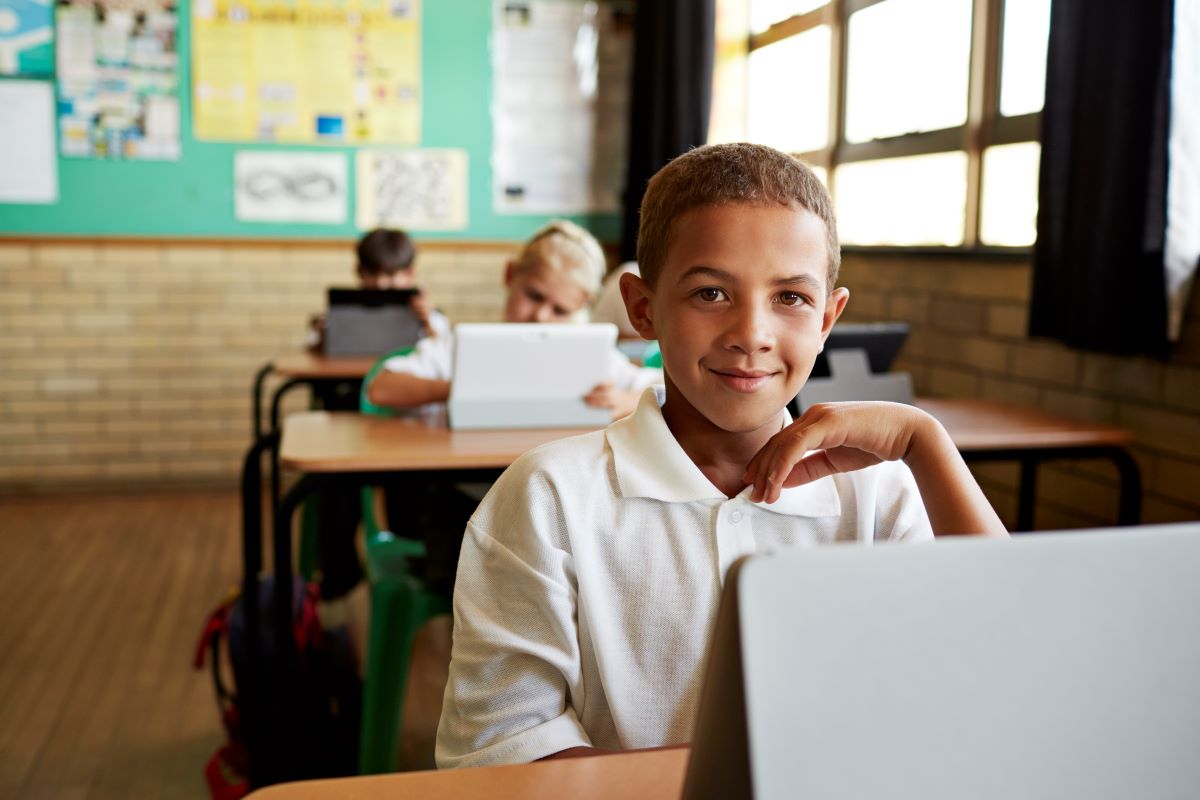 boy at a desk in a classroom with a tablet