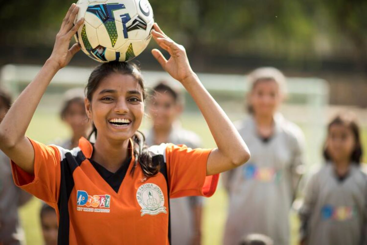 A South Asian teenager playing football with her team from different ethnicities.