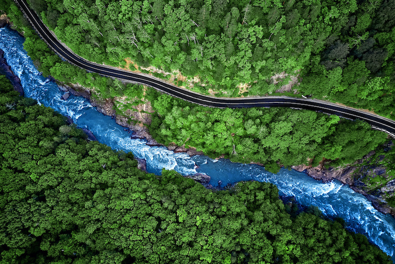 Aerial photo of a river running alongside a road through a forest 