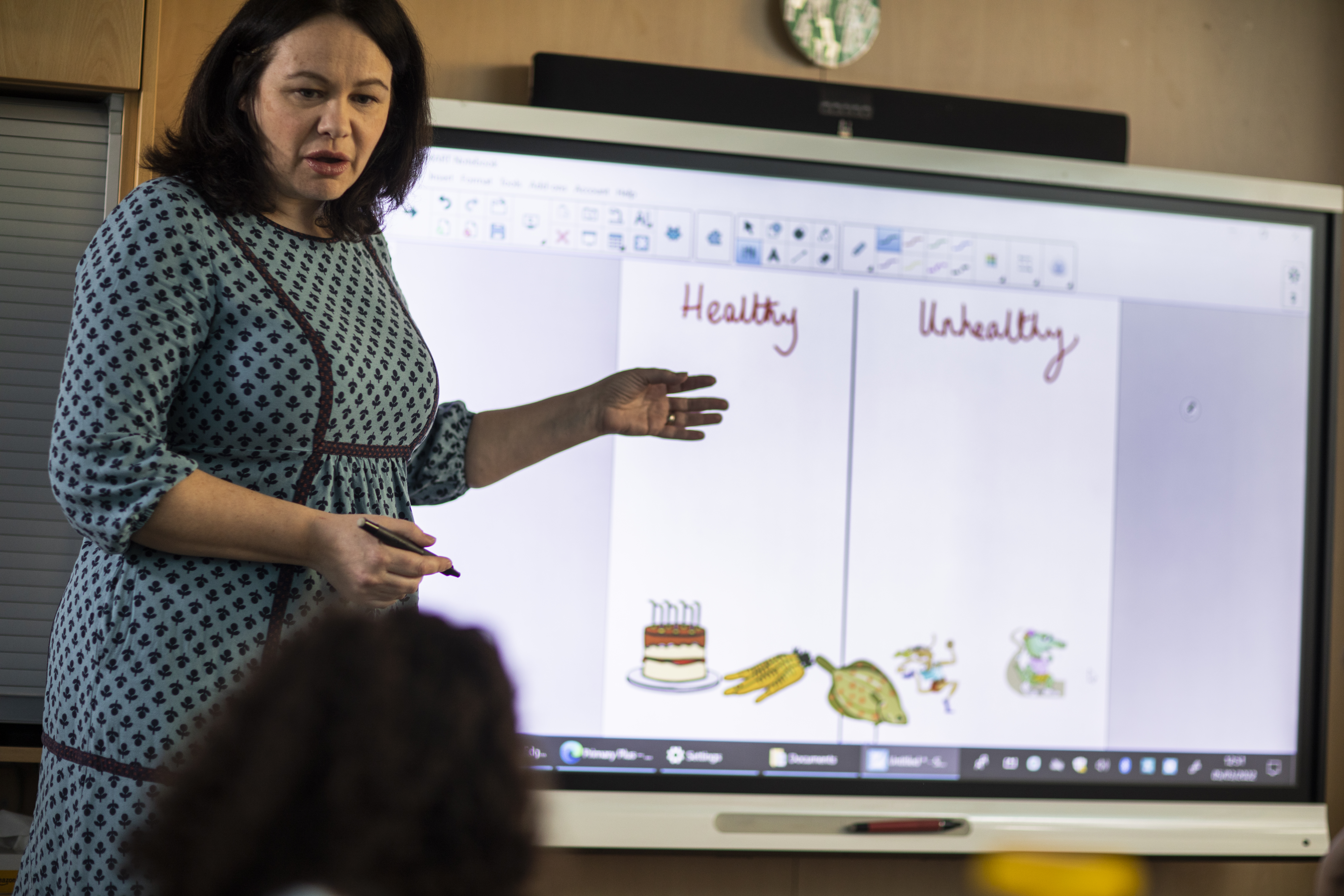 Teacher standing in front of whiteboard in young learner class