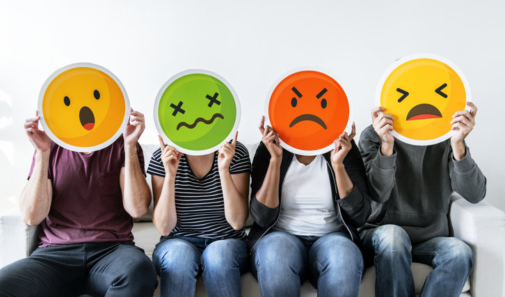 four people holding emoticons over their faces