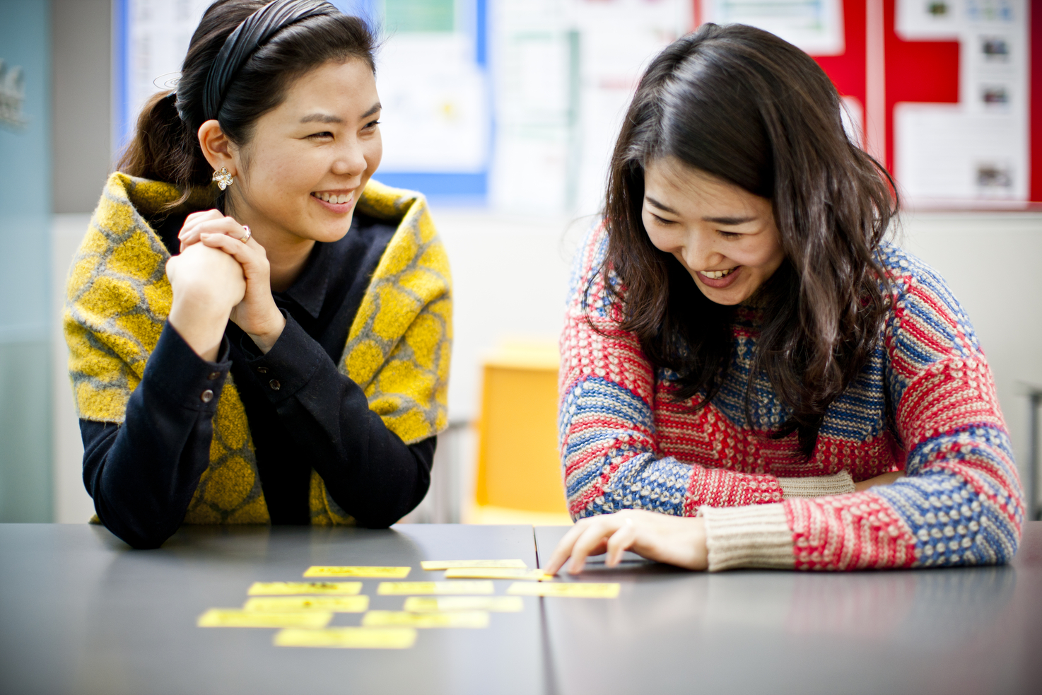 Two South Korean female teenage students smiling and sitting at a table looking at pieces of yellow paper