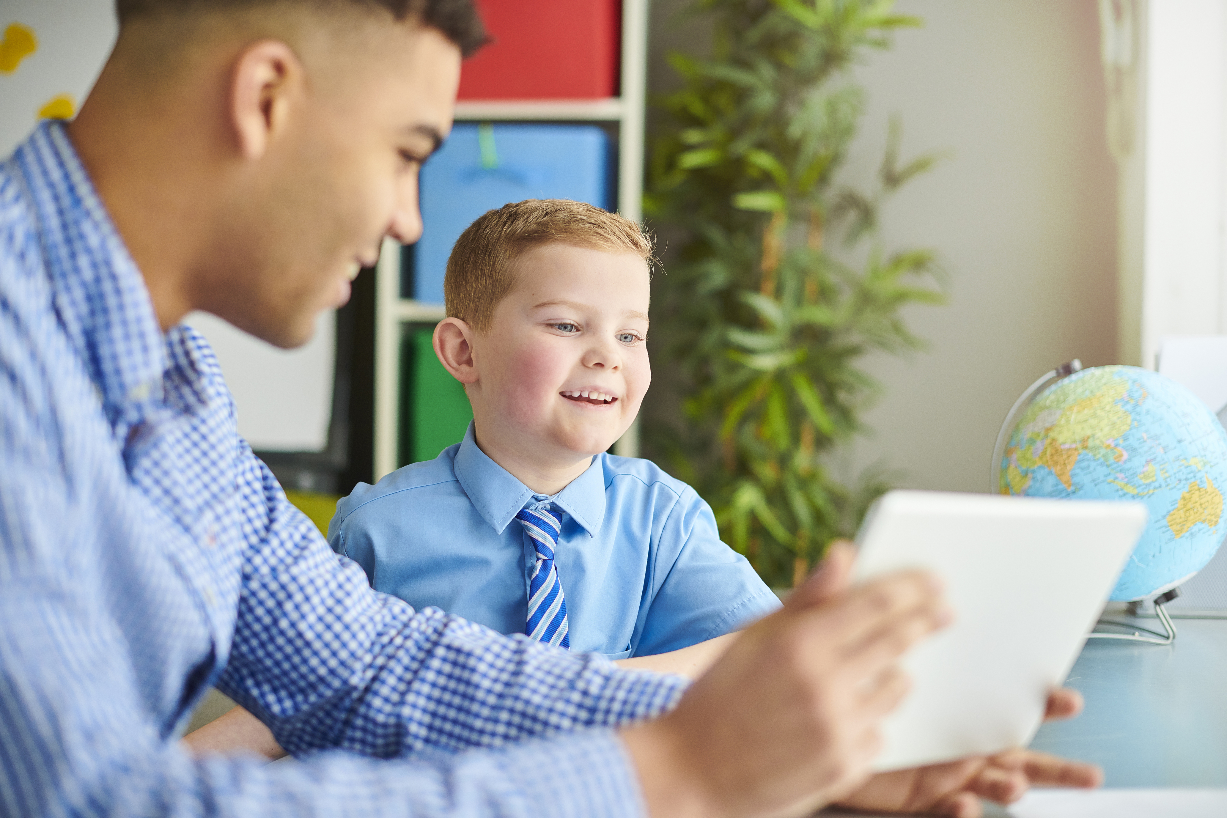 Young boy smiling while looking at a tablet with his teacher