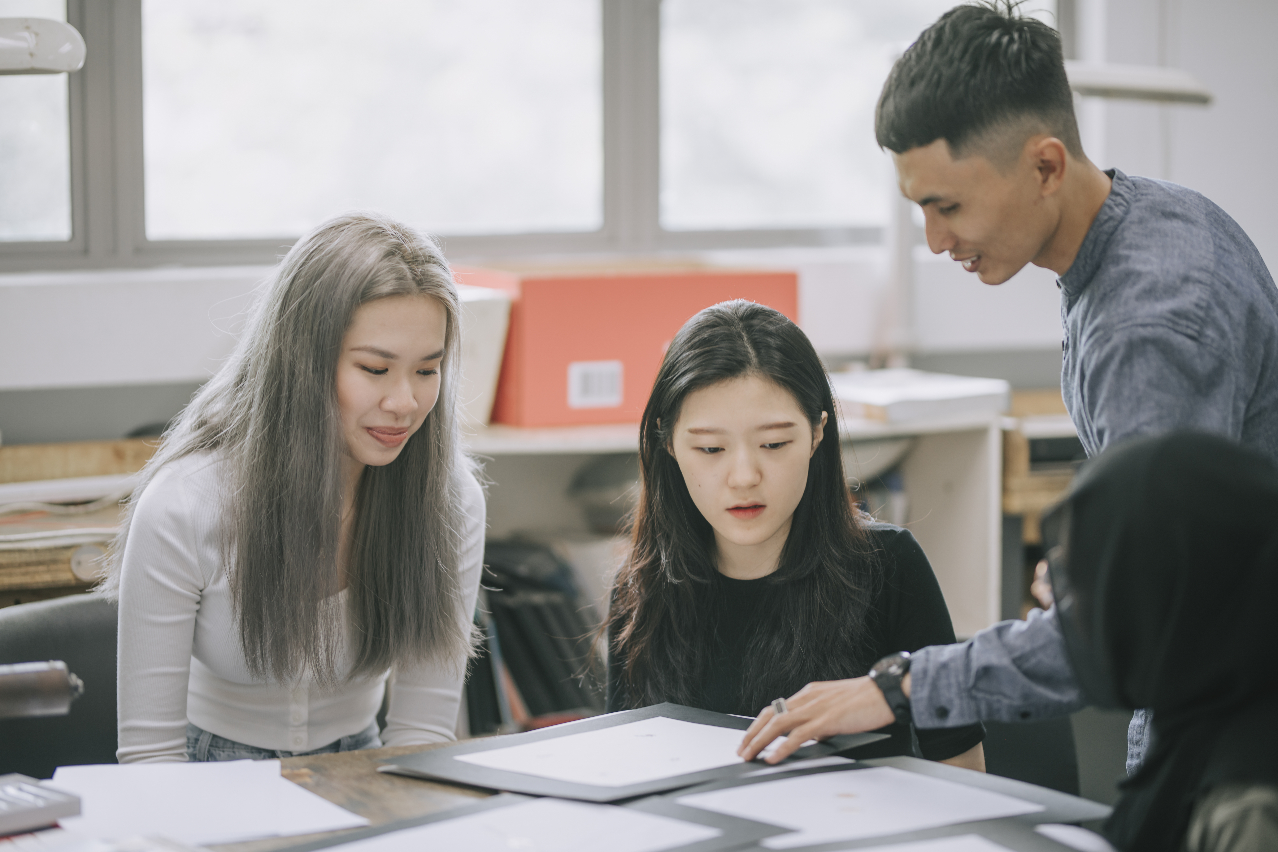 A group of Asian students look at some designs on paper