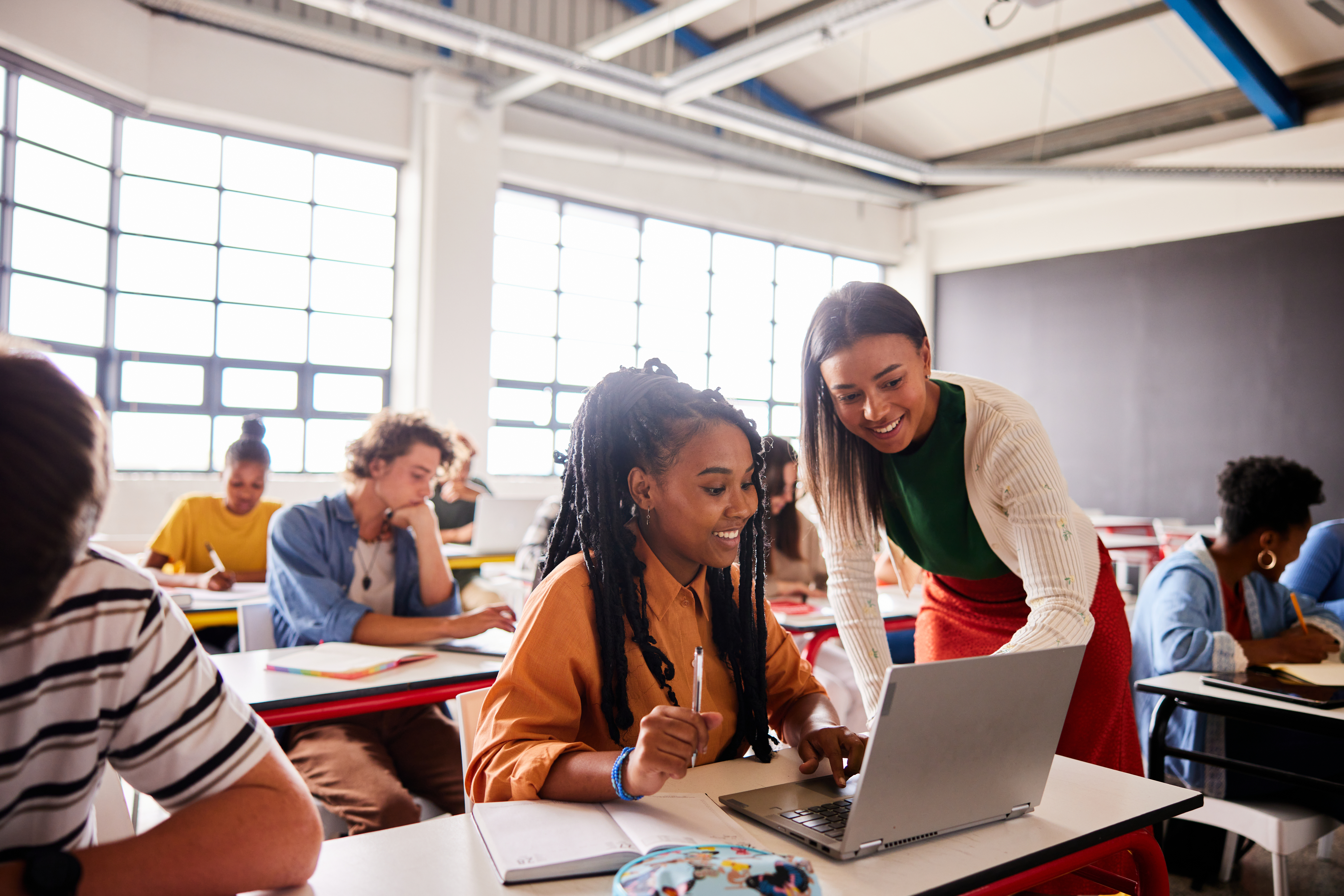 Smiling teacher standing over learner using a laptop