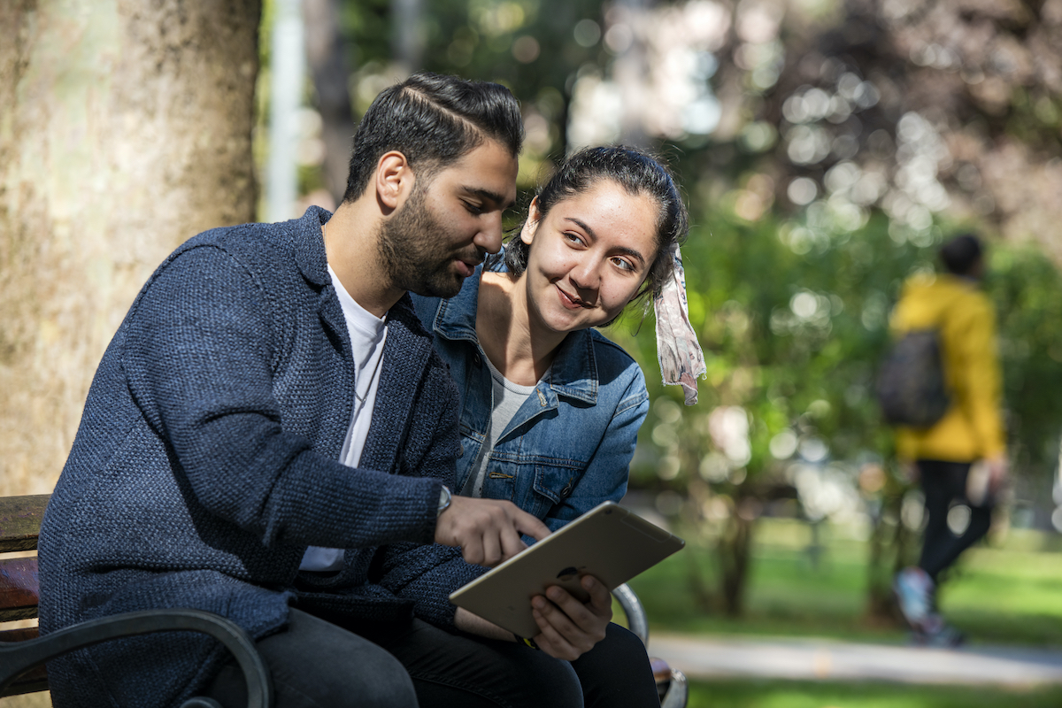 A male and female sitting in a park looking at a tablet computer