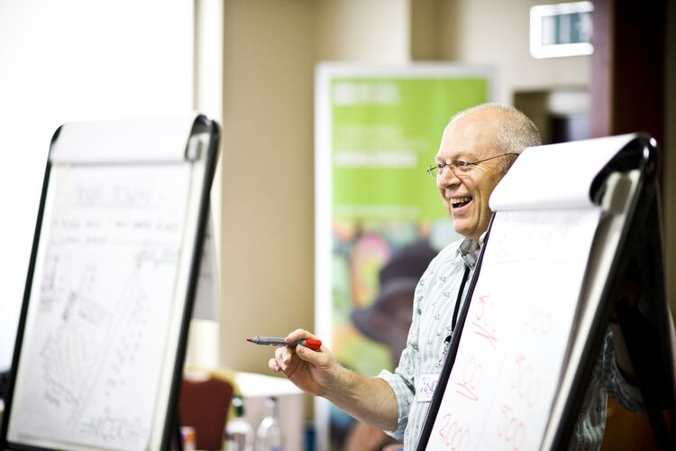 Older male teacher educator laughing, standing between two flip charts