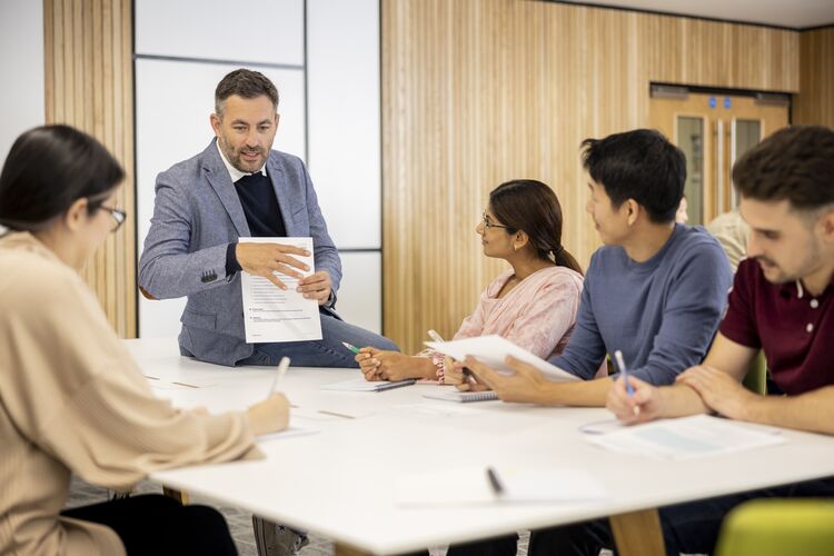 Teacher sitting on desk talking to adult learners