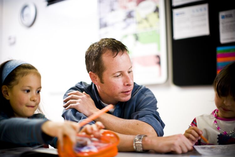 Teacher sitting at desk with two young learners