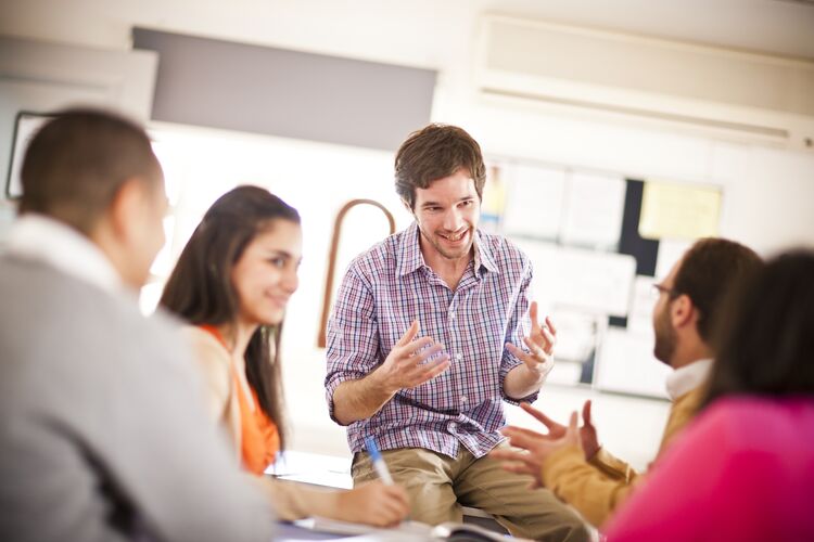 Teacher sitting on desk explaining something to students