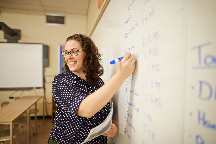 A teacher writing on whiteboard whilst looking at students