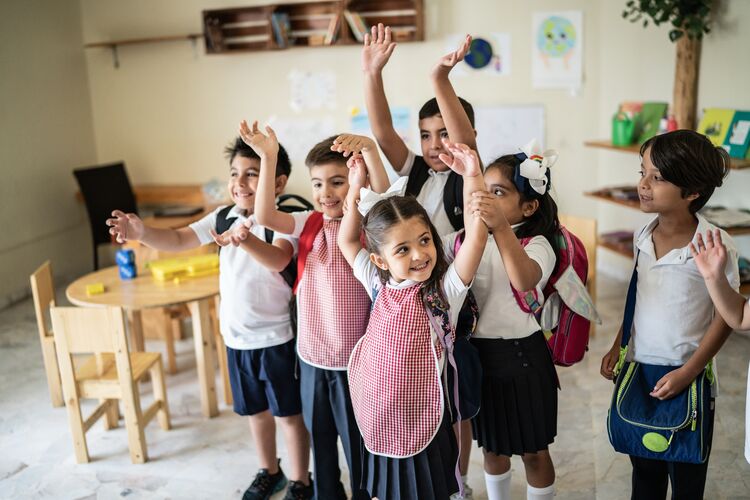 Diverse group of primary learners raising hands in classroom