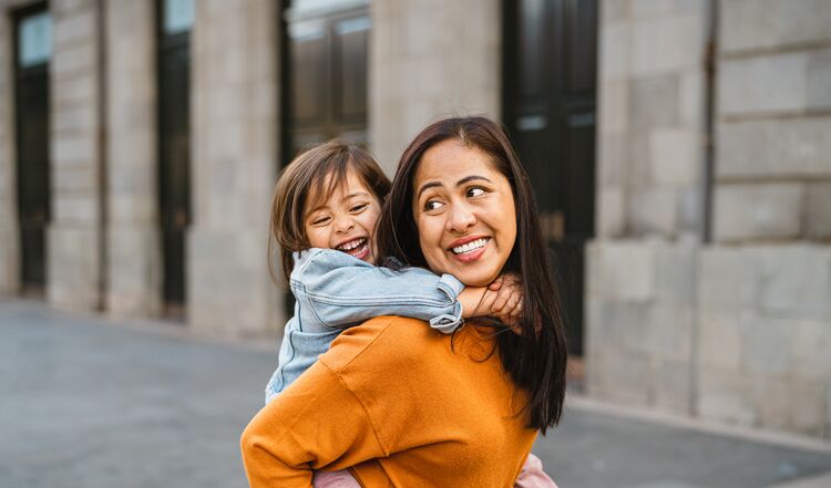 A young smiling Asian girl being carried by her mother on the street