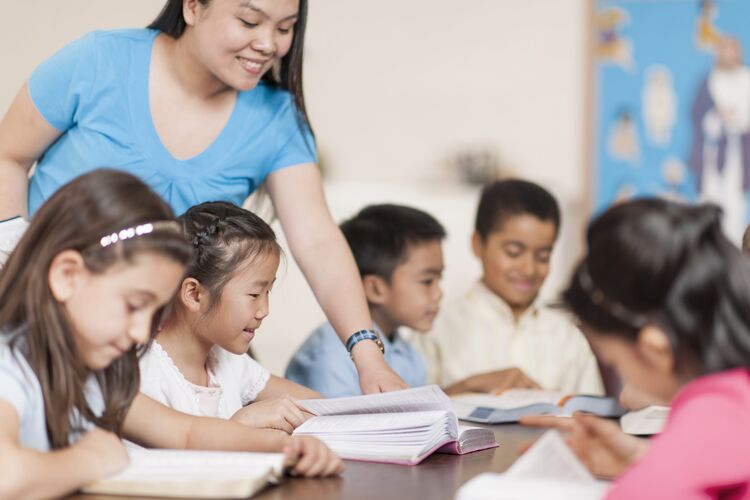 A teacher helping a group of young Asian learners with reading