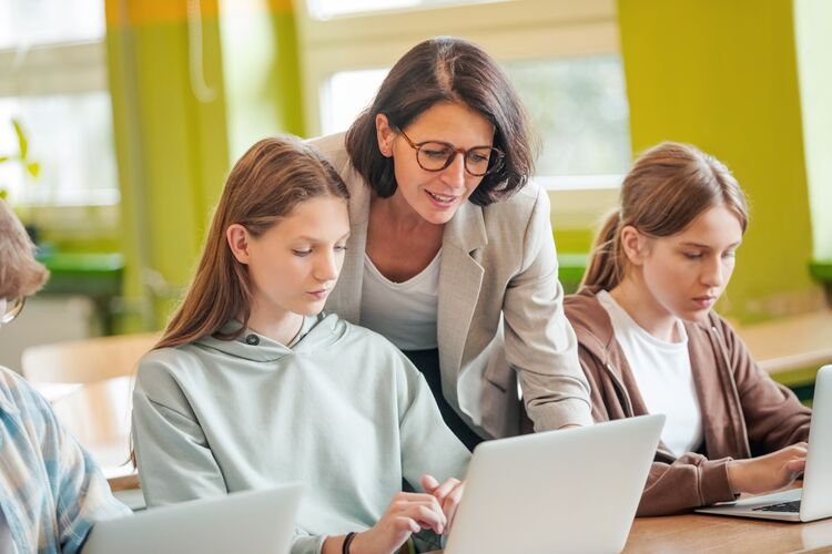 Teacher helping secondary students working on laptops