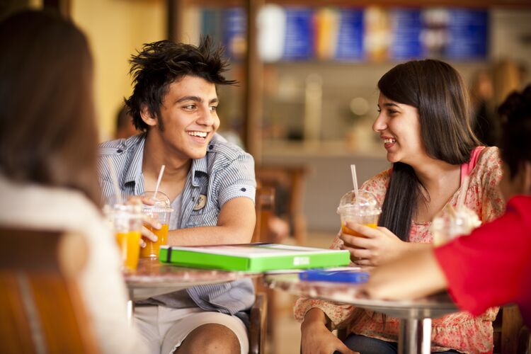 Two young adults - male and female - talking and smiling in an outdoor cafe