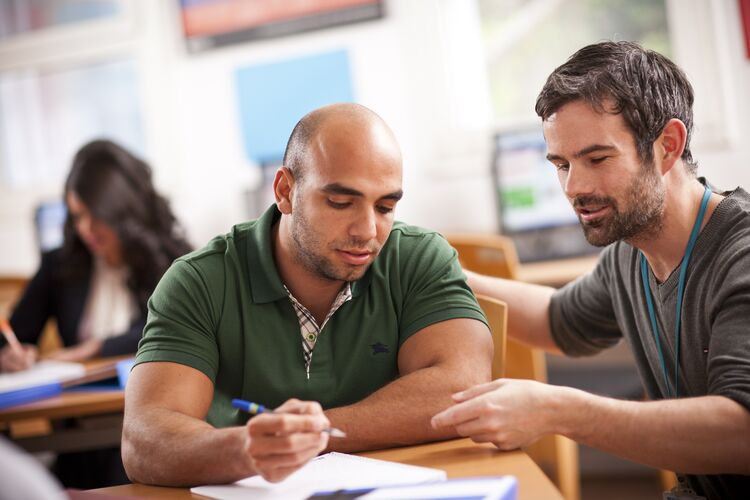 Teacher talking to a student at a desk in classroom in Kuwait