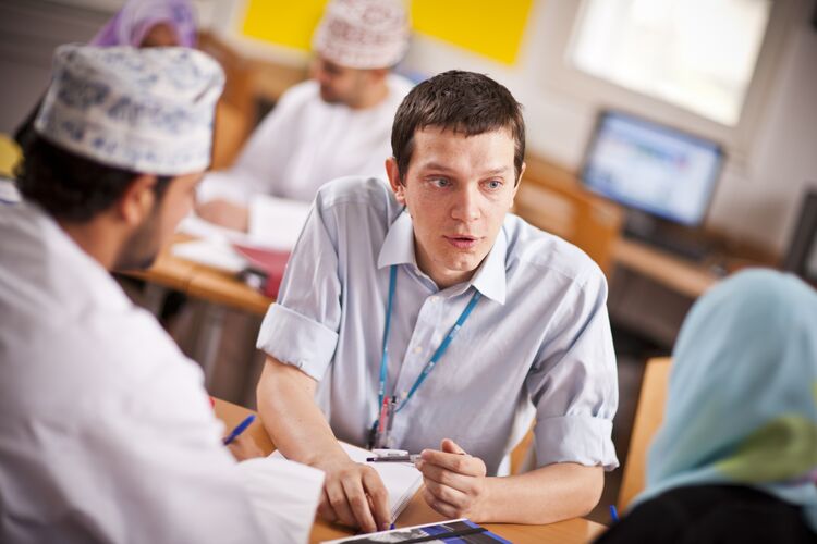 A teacher in Oman sitting at a desk correcting students