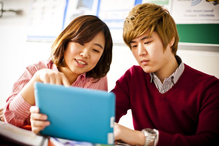 Two students in South Korea reading on a tablet