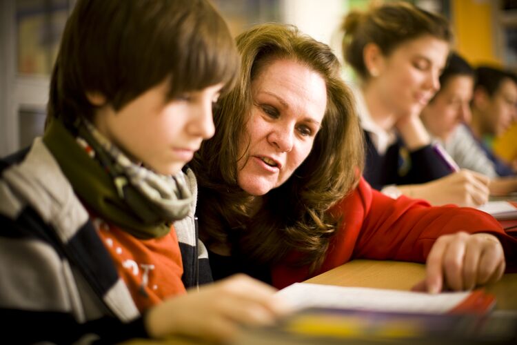 A teacher sitting with a learner pointing to a text 