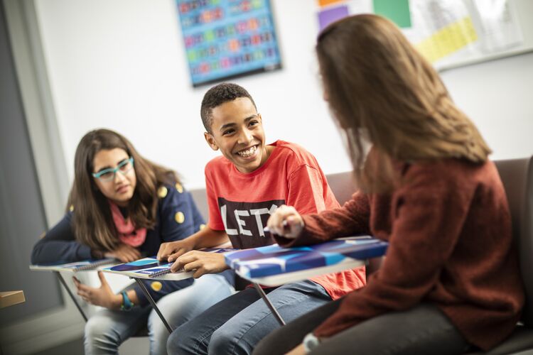 A pair of students talk together while another student listens