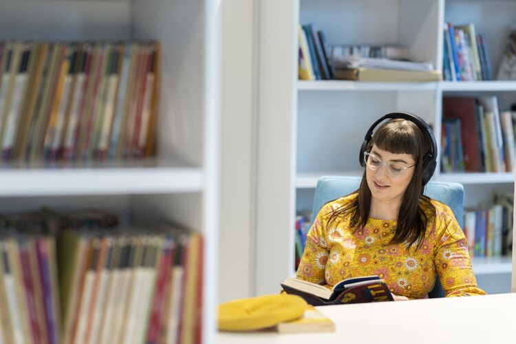 Woman reading with headphones on in a library