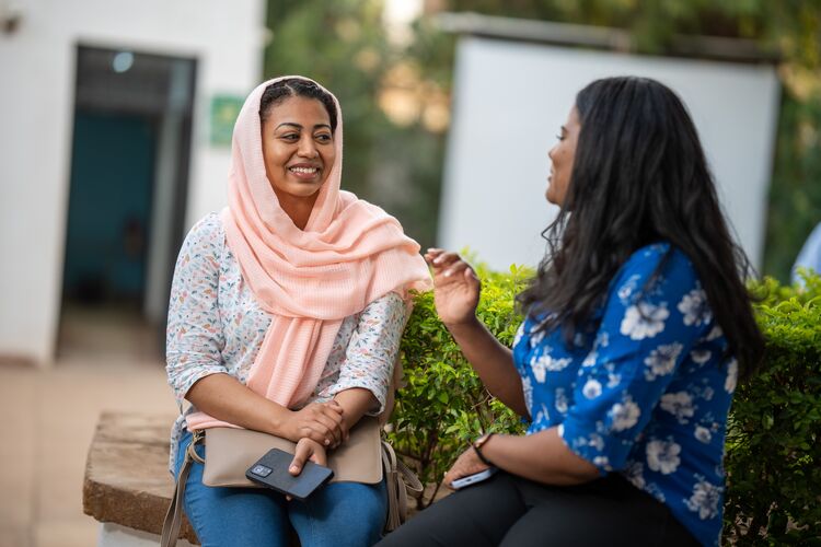 Two female teacher educators sitting outside talking and smiling