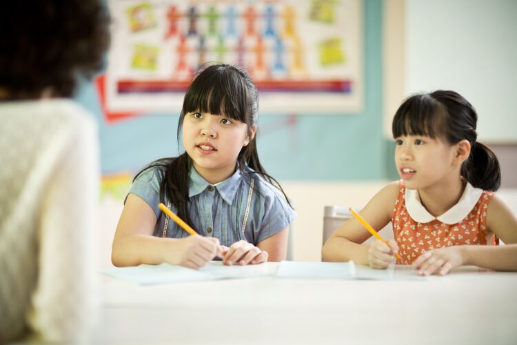 two Vietnamese young learners holding pencils and listening to a teacher 